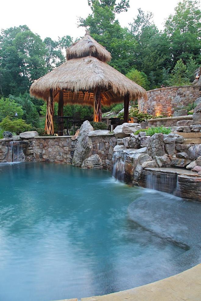 A coarse-made gazebo in a tropical style is highlighted with an artificial pond with small waterfalls